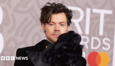 Harry Styles in a black designer jacket with over-sized flower detail at his neck, at the Brit Awards