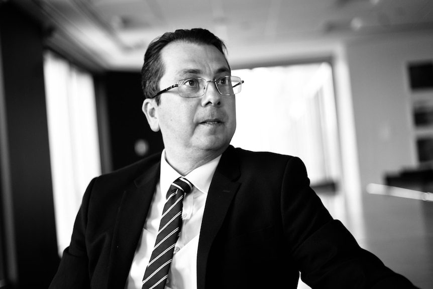 A black-and-white picture of a clean-shaven man in a suit, tie and glasses.