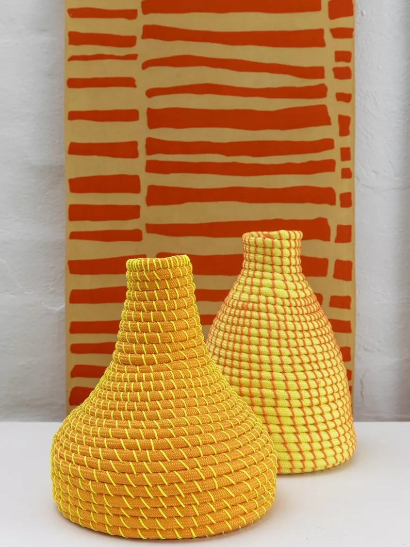 A textile artwork; two bright orange and yellow woven conical vessels.