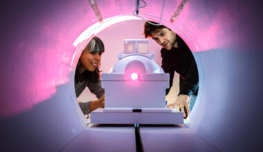 Two people look inside of an MRI machine. A pink light shines inside.