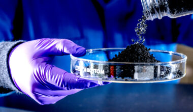 A hand in a latex glove holds a glass dish into which is poured particles of recycled tire rubber.