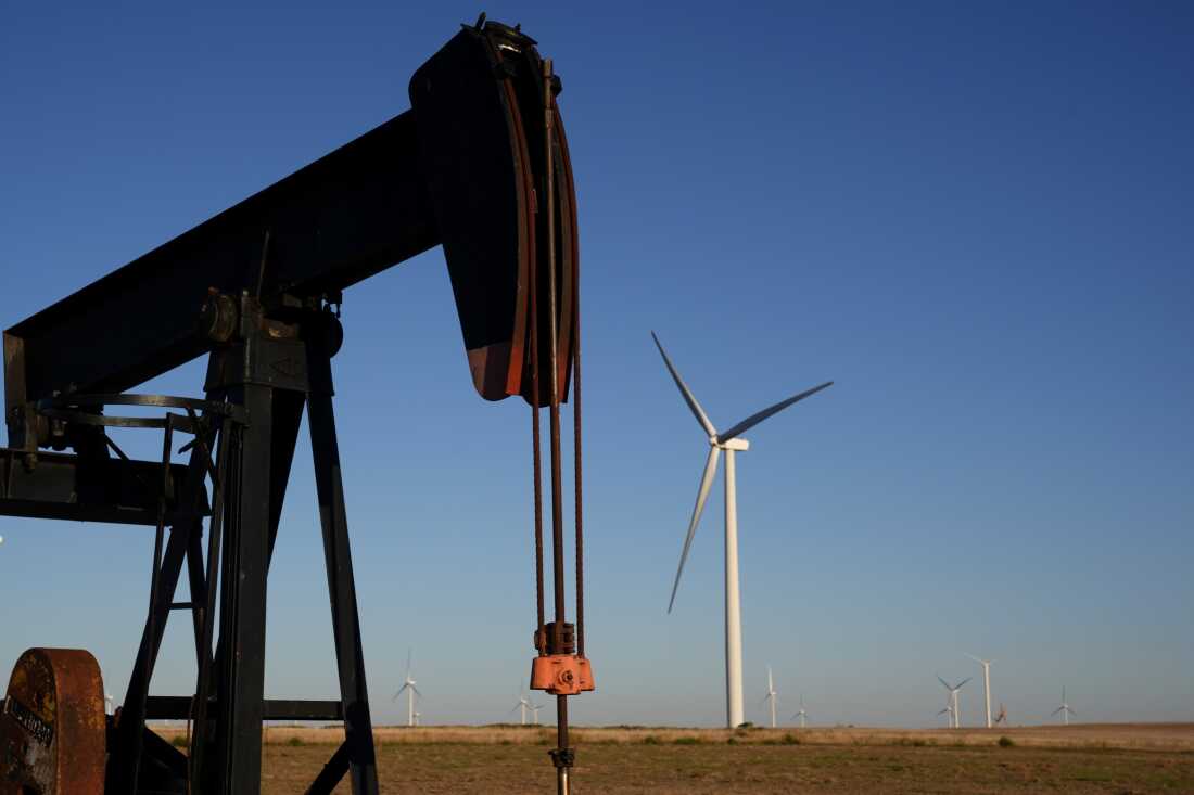 Pumpjacks operate in the foreground while a wind turbines at the Buckeye Wind Energy wind farm rise in the distance in Kansas.