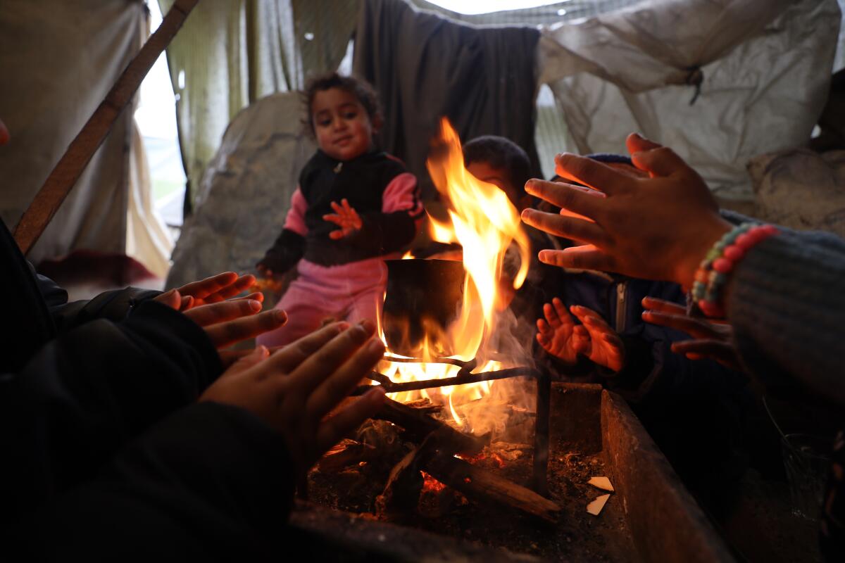 Palestinian children warm their hands around a bonfire in a makeshift tent