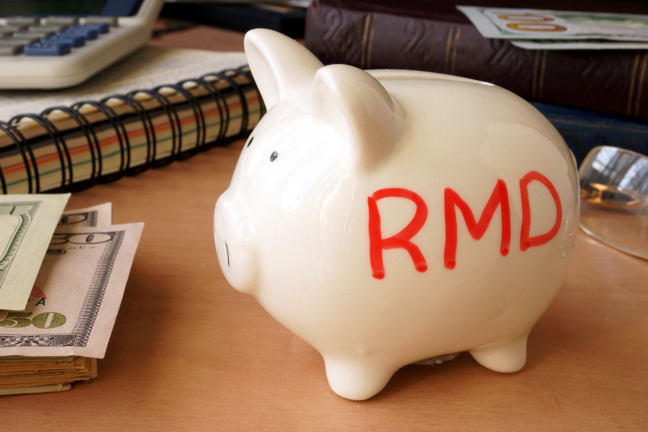 A piggy bank labeled "RMD" stands beside stacked U.S. currency.