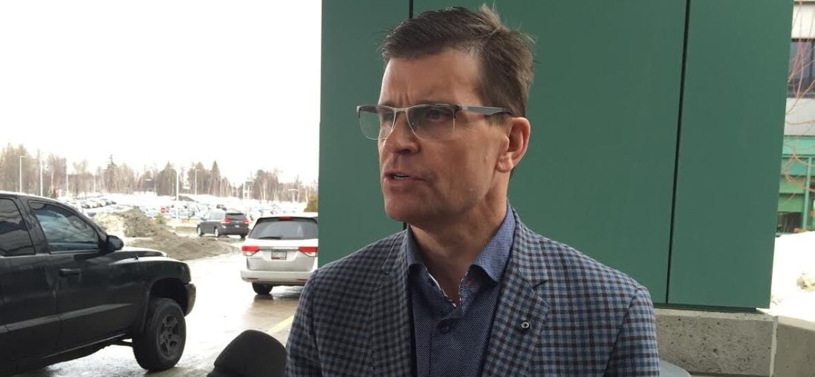 A man with glasses speaks into a microphone in a hospital parking lot