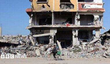 Rubble and a destroyed building as a man on his bike rides past it on a dirt road.