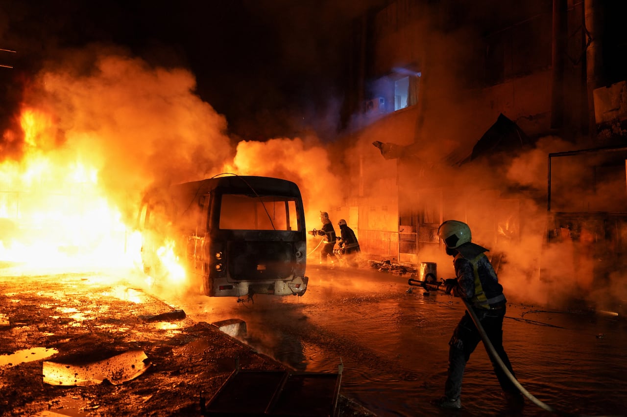 People work to extinguish a fire on a street where a bus is damaged.