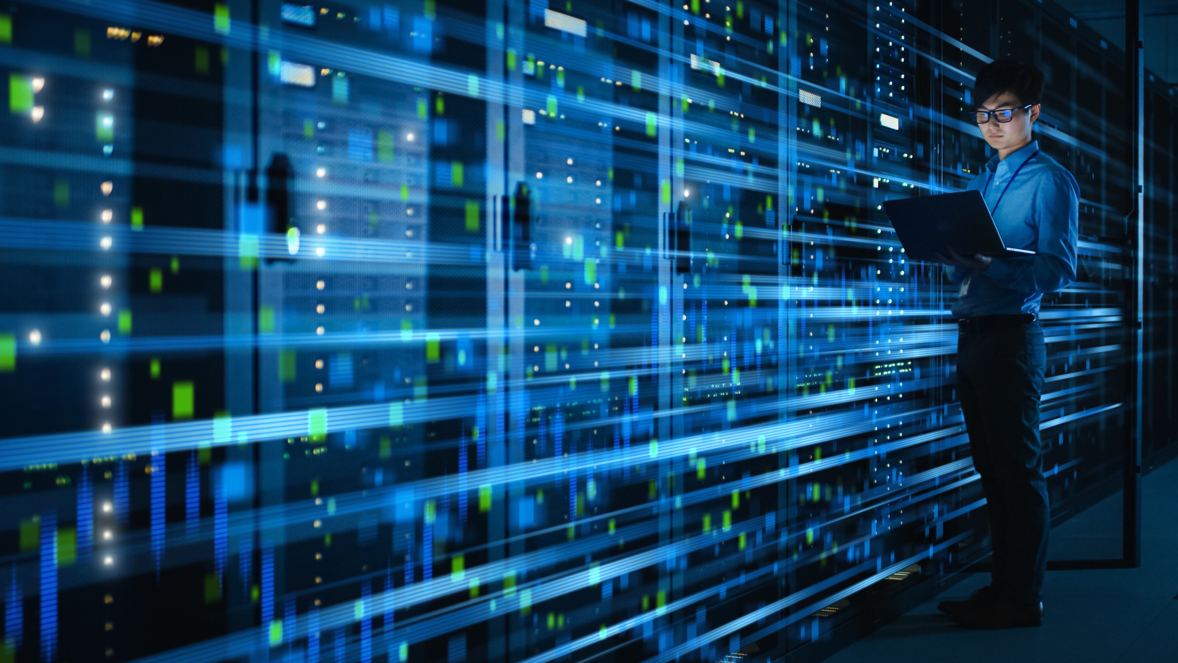 Server stacks in a data center with blue lights and worker on laptop in front. 