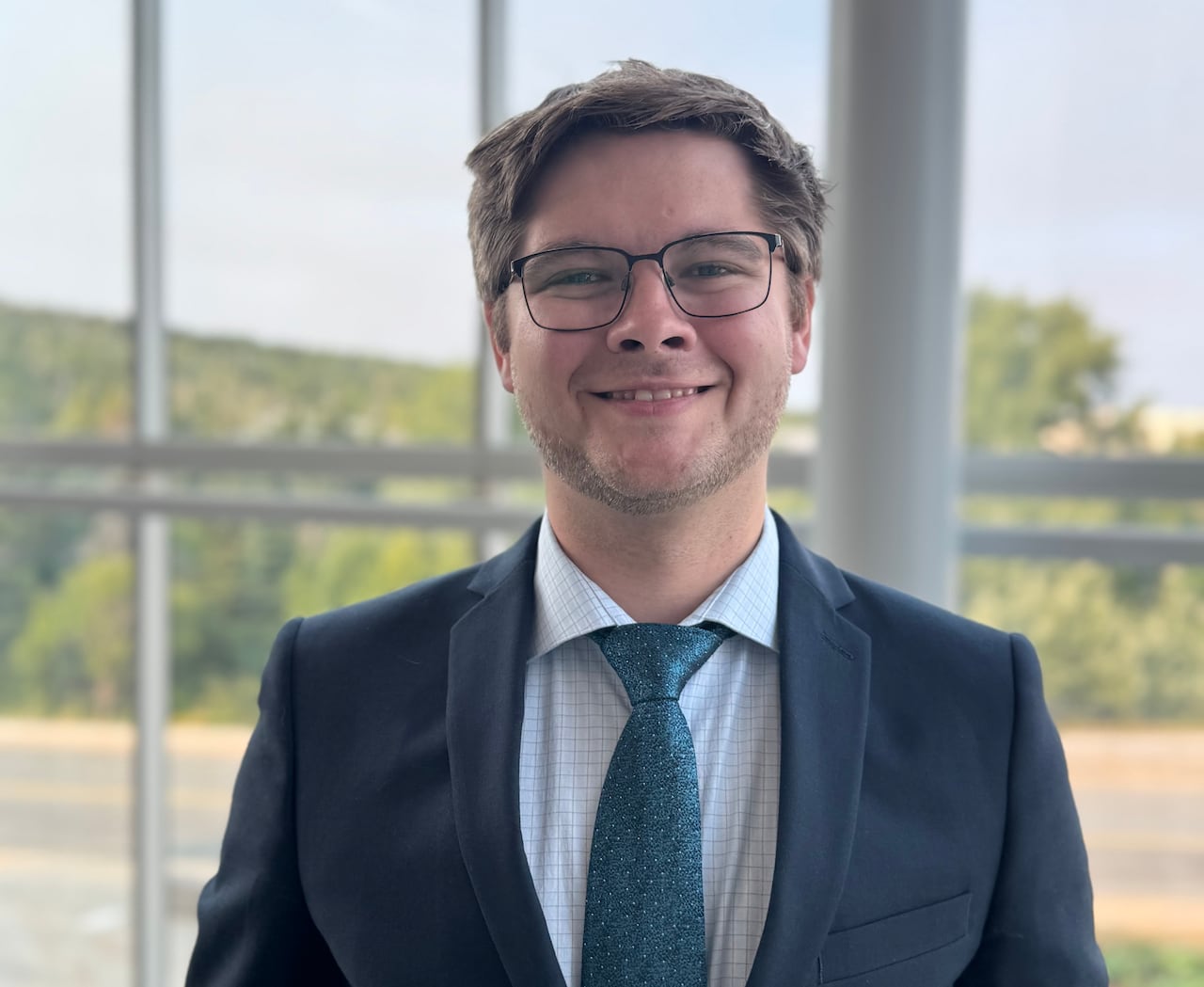 A man in a suit smiles for the camera in front of a window.