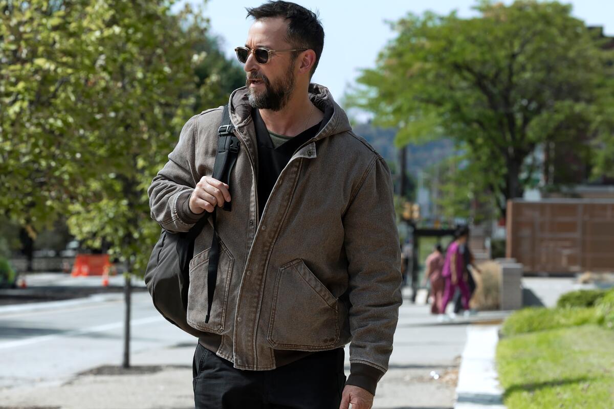 A man in sunglasses and a puffy jacket walks on a sidewalk