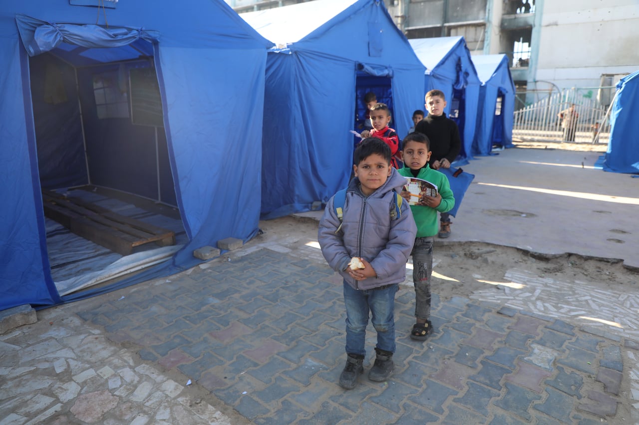Little boys in winter coats line up on the pavement outside blue tents
