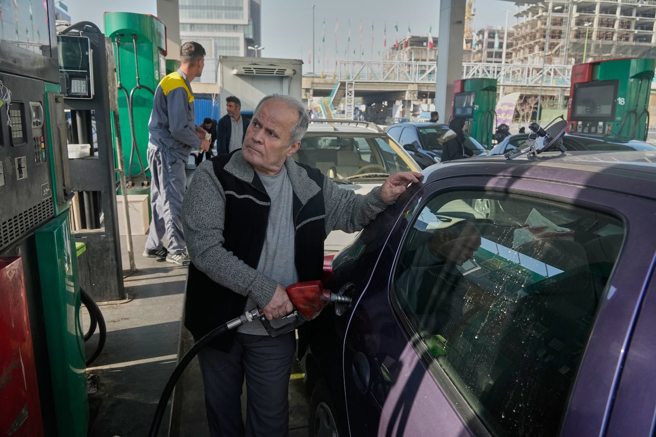 A crowd of people fill their cars at a busy gas station