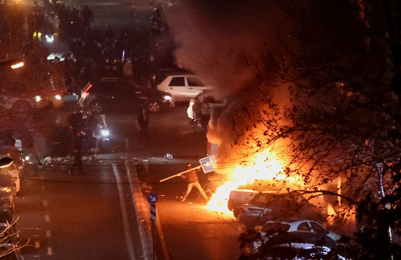A person throws a street sign into a fire on a dark street