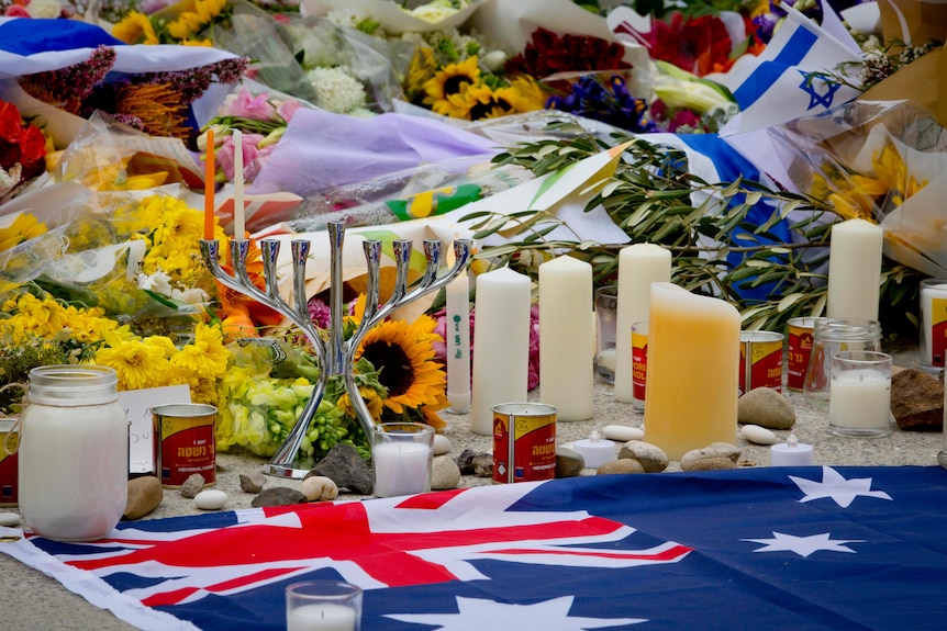 A menorah stands amount candles, flowers and an Australian flag at a memorial to the victims of the Bondi terror attack.