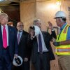 This photo shows President Trump, Federal Reserve Chair Jerome Powell and the director of the Office of Management and Budget, Russell Vought, during a tour of renovations at the Federal Reserve in Washington, D.C. Powell is speaking with the construction manager, who is wearing a fluorescent vest. Wooden boards cover many areas of the building.