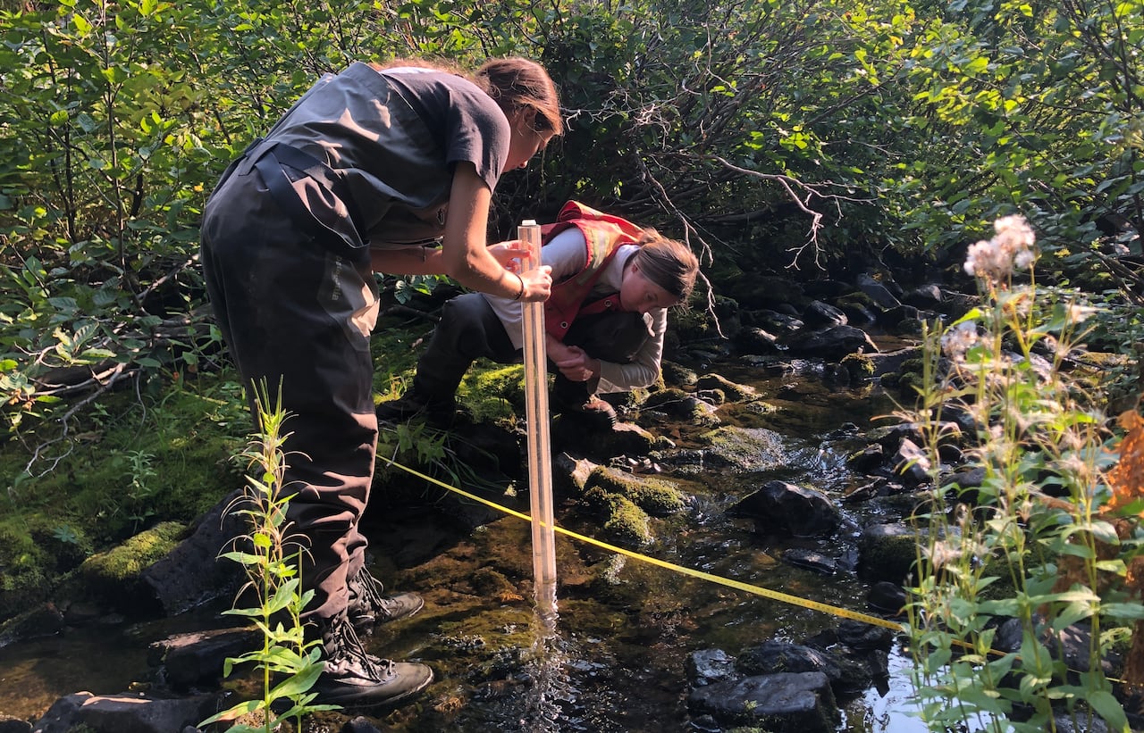 Two women measure water levels in a creek.