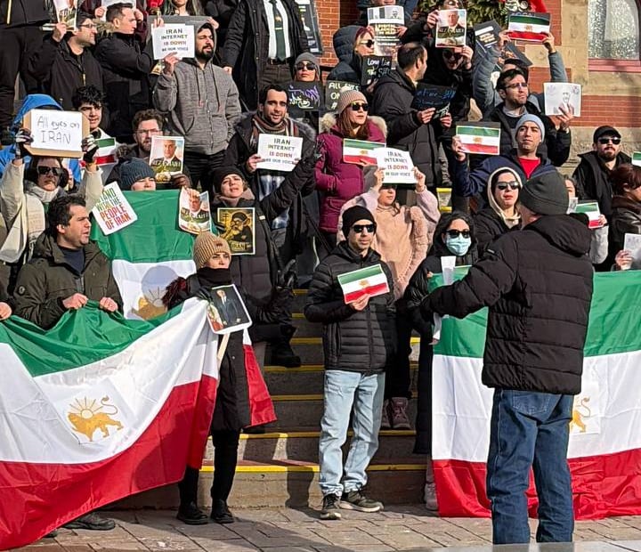 Supporters standing on the steps of a building holding up Iran flags.