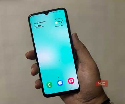 Person holding Samsung phone showing clean home screen with clock and weather