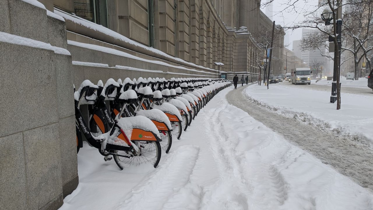 Line of bikes are covered in snow.
