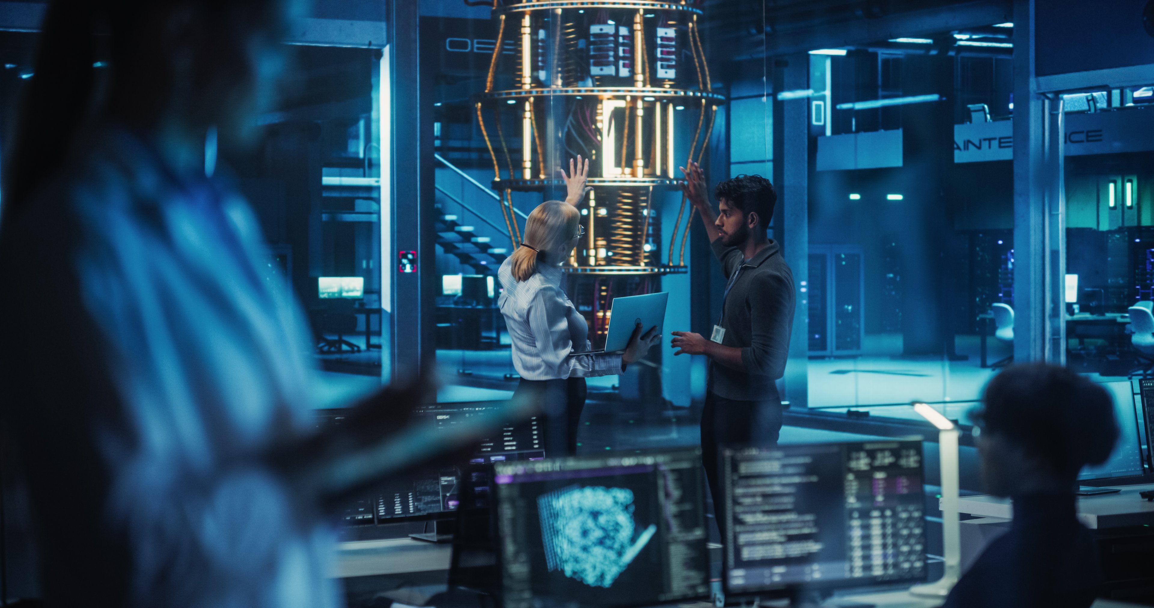 Two people standing by and working on a quantum computer with two other people in the foreground.