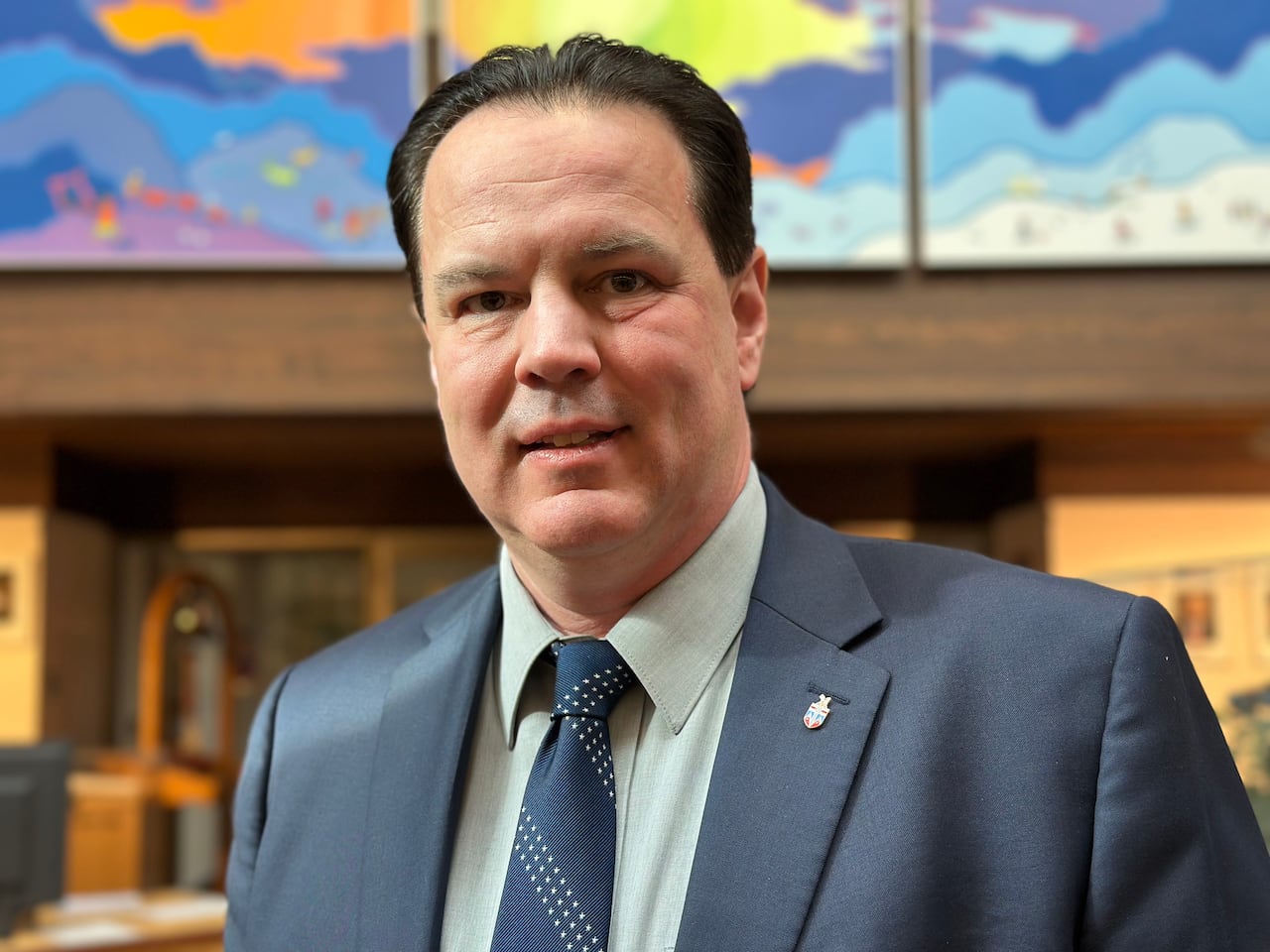 A portrait of a man with dark hair in a navy blue suit.