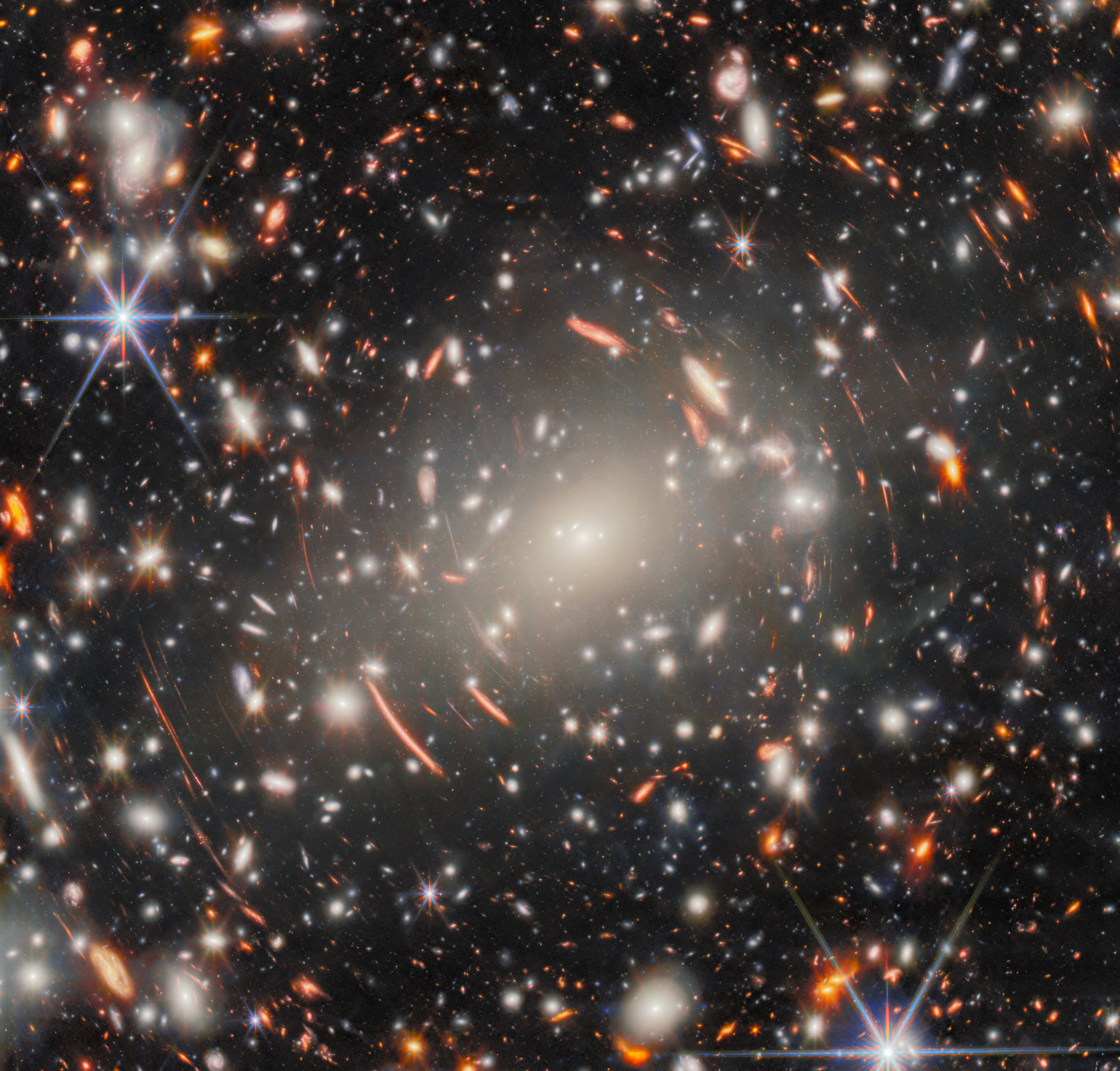 A dense field of distant galaxies, with bright stars and orange arcs of light, illustrates gravitational lensing in deep space, as the JWST reveals new details about our universe.