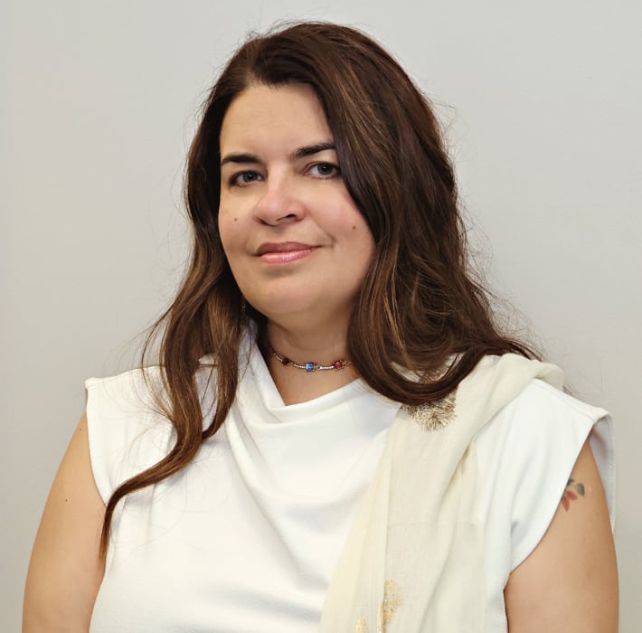 Headshot of Caroline Lidstone-Jones wearing a white top, white scarf and beaded necklace.