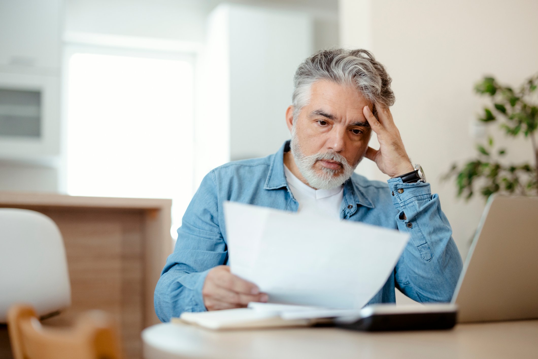 A person at a laptop with a serious expression holding a document.