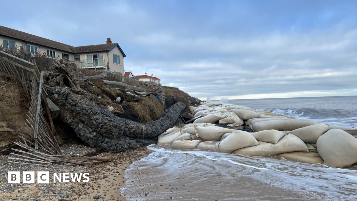 A home on the edge of an eroding cliff in Thorpeness. There is a big cluster of geobag sea defences on the beach in front of it. The tide is washing in.