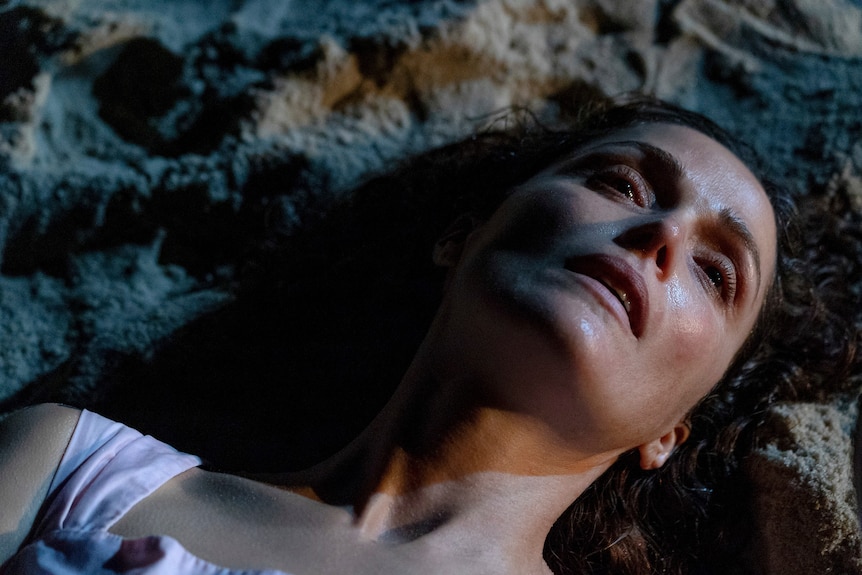 Actor Rose Byrne lies on sand in the dark in a scene from a film.