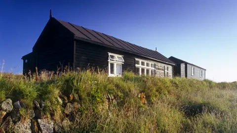 National Trust A wide shot of the radio station. It is a brown single-storey hut surrounded by grass.
