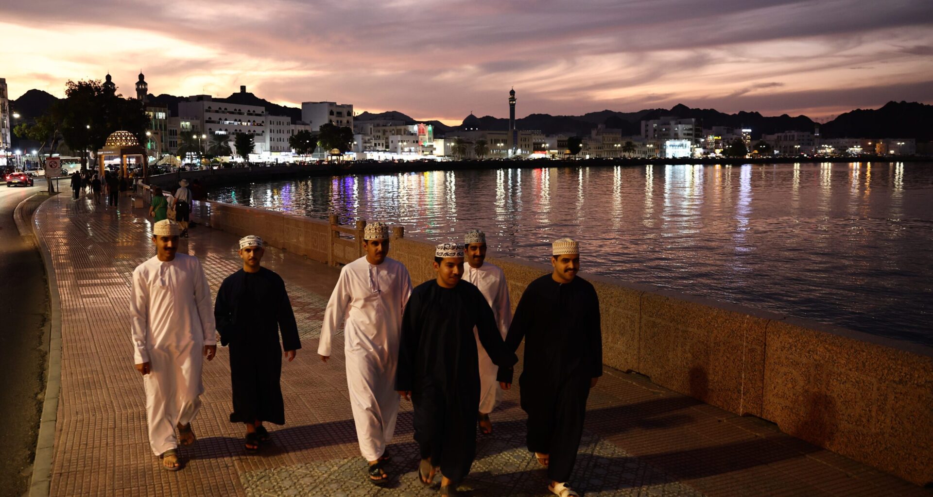 People wearing traditional clothing walk the Mutrah Corniche in Muscat, Oman. The government plans to boost growth and spark job creation in 2026