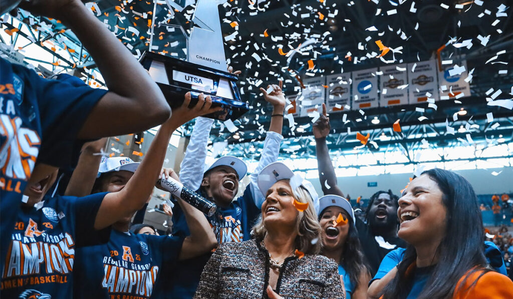 UTSA women's basketball players lift the conference championship trophy as confetti falls