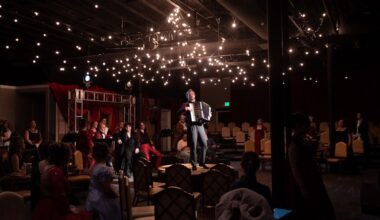 People watching an actor play the accordion in a theater-in-the-round.