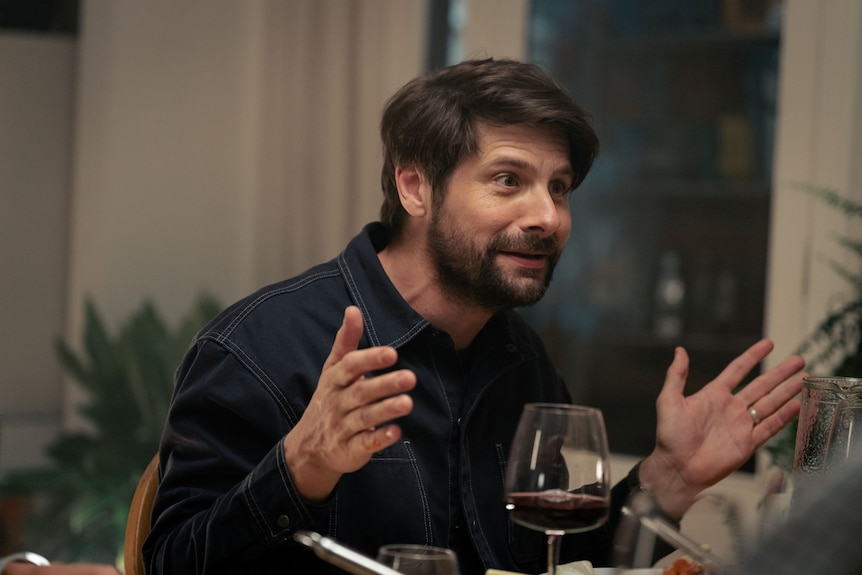 A TV still of Ryan Johnson, mid-40s, at a dinner table. He's talking, smiling slightly, gesticulating for emphasis.