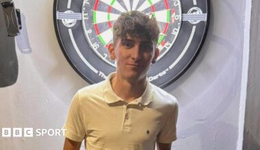 Tyler Thorpe poses in front of a dartboard