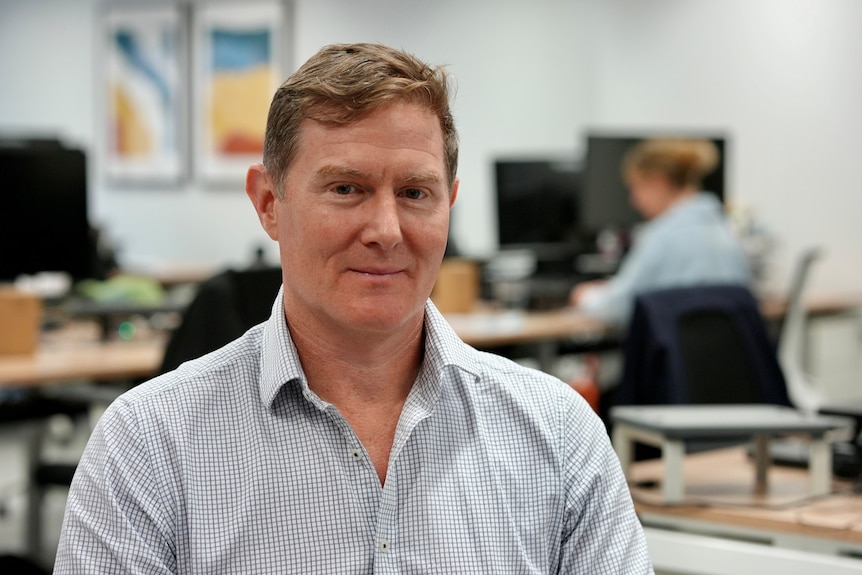 Man in a white shirt with a check pattern sitting in an office.