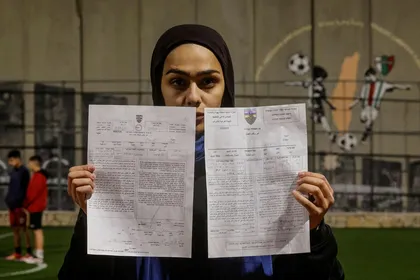 A Palestinian teen holds the demolition order of the football field, next to the West Bank barrier separating Aida refugee camp from Israel.