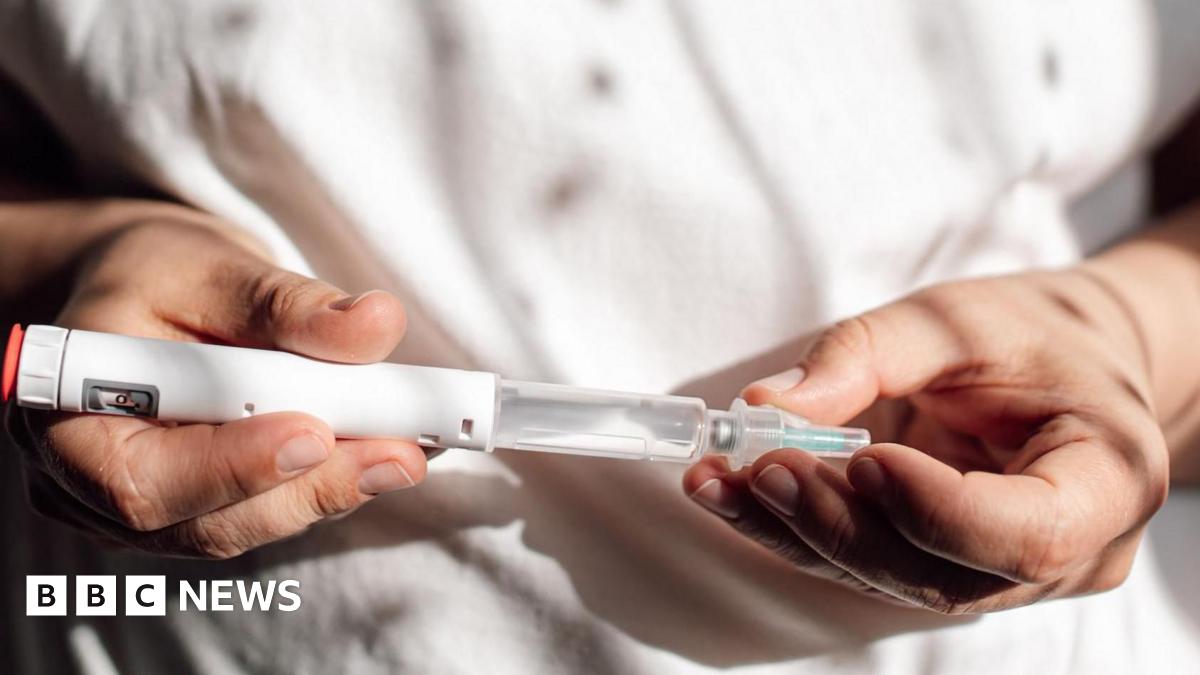 A close up of a health professional, in white clothing. They're holding a weight loss drug - in the form of a tube or syringe - that is ready to be injected.
