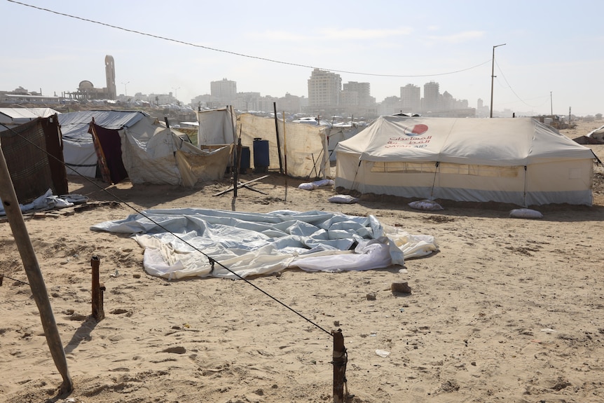 A flat tarp and unpitched tent on the sand surrounded by other tents