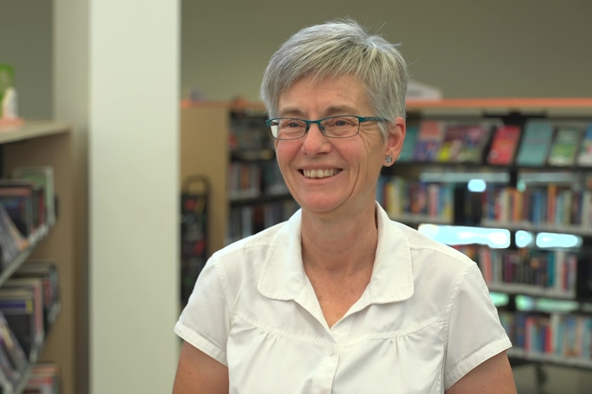 A woman smiles standing next to book shelves