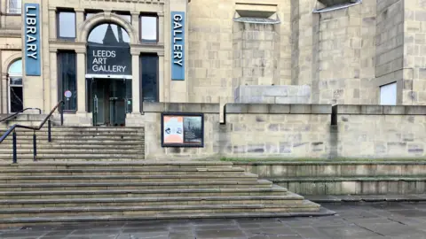 Alex Moss/BBC The entrance to Leeds Art Gallery, built from light stone. Stairs lead up to the door. 