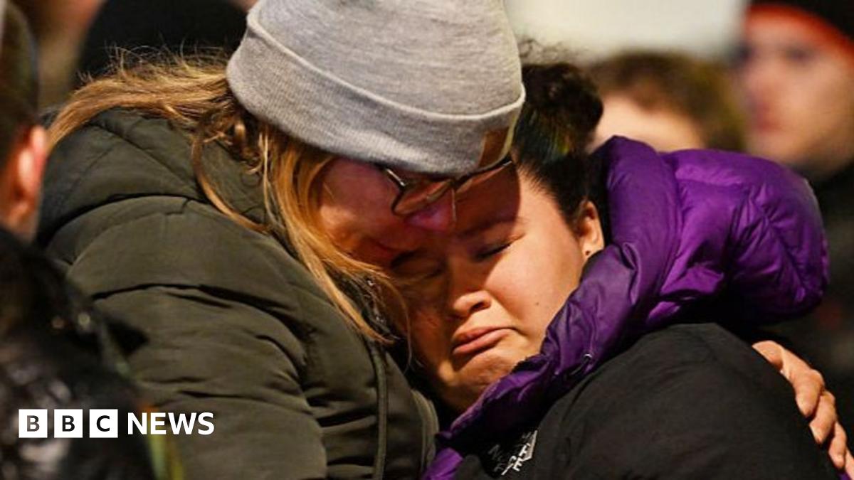 People gather at the scene of a deadly bar fire in Switzerland. They are stood in front of a huge pile of flowers and candles.