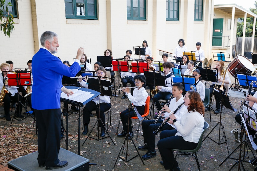 Garry Clark wears a bright suit jacket and conducts a junior brass band.