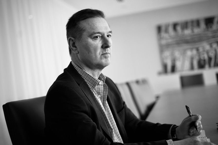 A black-and-white photo of a man in a jacket, sitting at a desk.