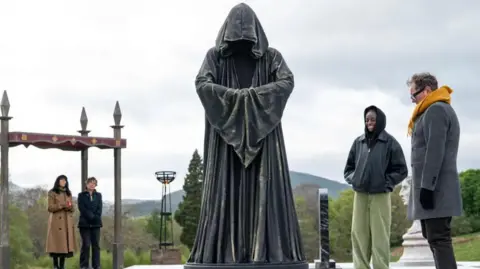 BBC/Studio Lambert A giant cloaked chess piece with celebrities looking on on The Celebrity Traitors