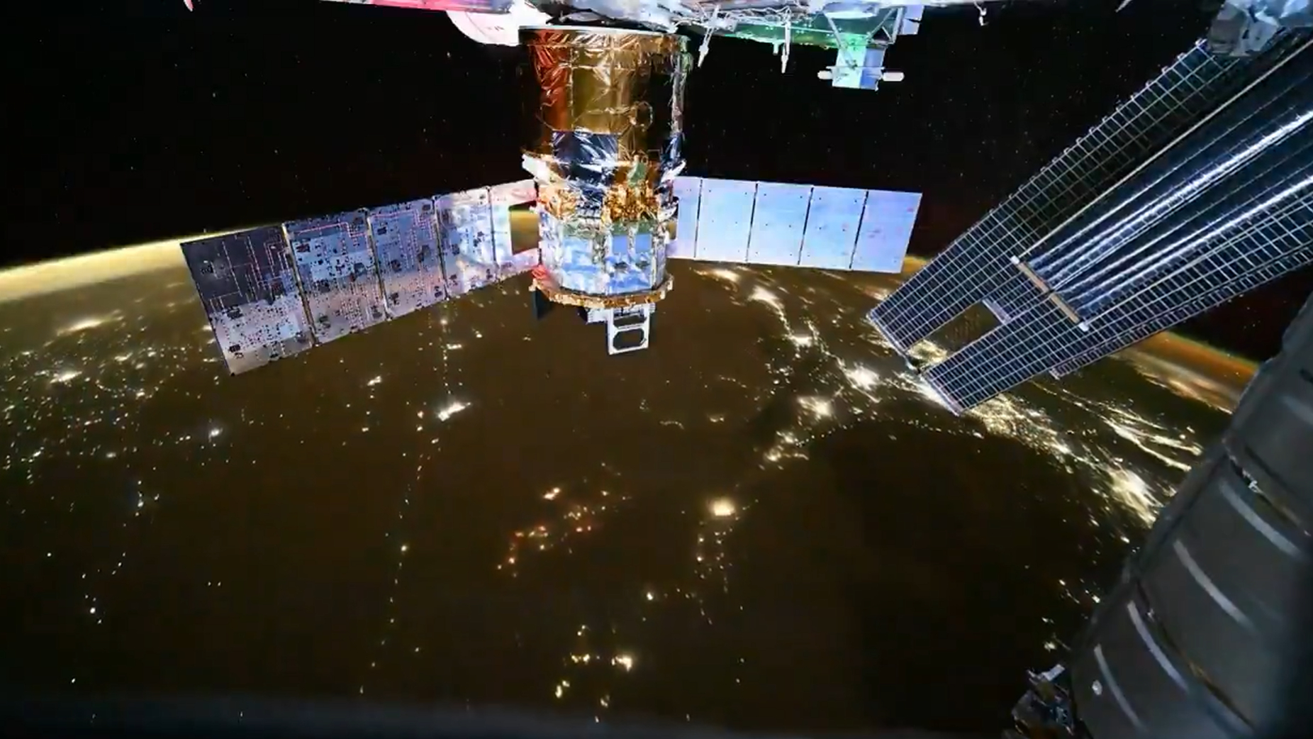 a gold foiled spacecraft hangs above earth. large solar panels enter the frame from the right.