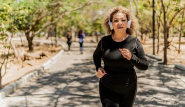 woman dressed in black sleeved top and leggings running outside with white headphones. she's on a path with trees and other people blurred in the background
