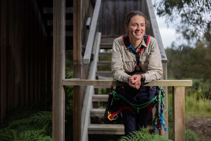 A woman with a tree climbing harness rig on posing for a photo.