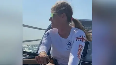 Call to Earth Emma Wolstenholme on board the crew's small rowing boat, looking to her right, wearing shades and clasping an oar